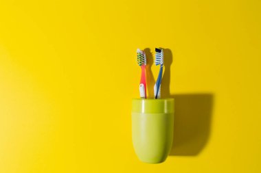 Sarı arka planda yeşil bardakta iki diş fırçası. Kırmızı ve mavi diş fırçaları. Caries 'e karşı koruma. diş sağlığı kliniği.