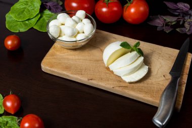  Yemek Geçmişi. Tahta bir tabakta fesleğen, domates ve acı biberle dilimlenmiş büyük bir mozzarella peyniri topu. Eski arka planda. Bedava fotokopi. Üst Manzara. menü tasarımı kavramı