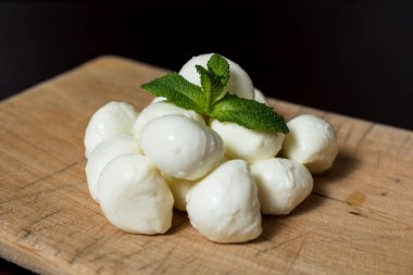 Tahta tahtada fesleğen yapraklarıyla süslenmiş küçük mozzarella peyniri topları. menü tasarımı kavramı.