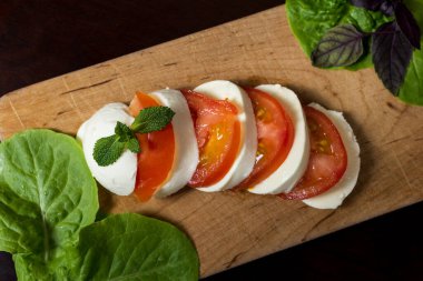  Yemek Geçmişi. Dilimlenmiş mozarella peyniri ve fesleğen yapraklı ahşap bir tabakta dilimlenmiş domates. Üst Manzara. menü tasarımı kavramı