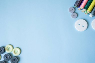 Düğme bolluğu, çok renkli iplikler, mavi arka planda iğneler. Aksesuar dikiyorum. reklam afişi.