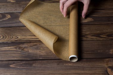 Ahşap bir masanın üzerinde bir rulo kağıt. Paketleme için kağıt. Kadın eli bir rulo kağıt sarar..