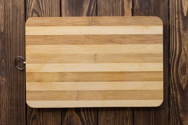 木製のテーブルの上には 薄暗い木やリングに縞模様の表面を持つ木製のまな板 チーズを切るための傷を持つ使用済みボード — ストック写真