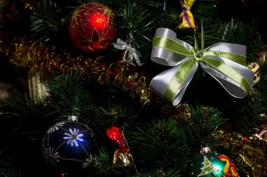 Noel arifesi. Farklı renklerde güzel Noel ağacı süslemeleri, çelenkler, yeşil ve beyaz renkli ipek kumaştan yapılmış bir Noel yayı. Ağaçtaki altın süslemeler.