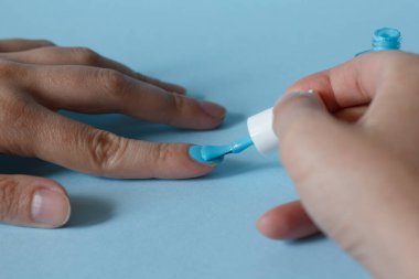 Tırnak bakımındaki kadın. Bir manikürcü bir kızın tırnaklarını mavi arka planda mavi tırnak cilası ile boyuyor. Manikür salonu. Manikür ve pedikür. reklam afişi.