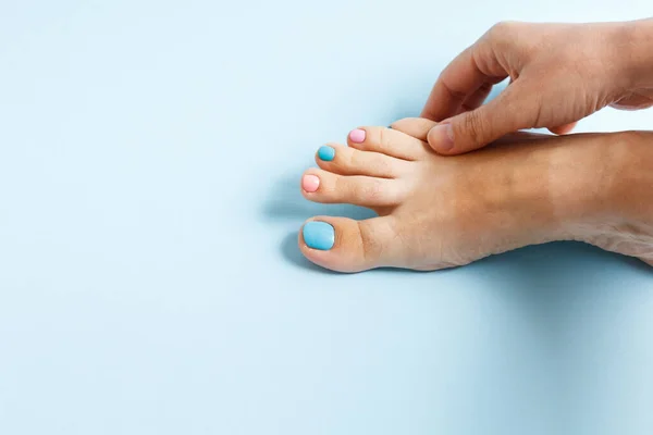 Female feet at spa salon on pedicure procedure. female leg with nails painted with multi-colored nail polishes on a blue background. nail care salon. manicure and pedicure. advertising poster.