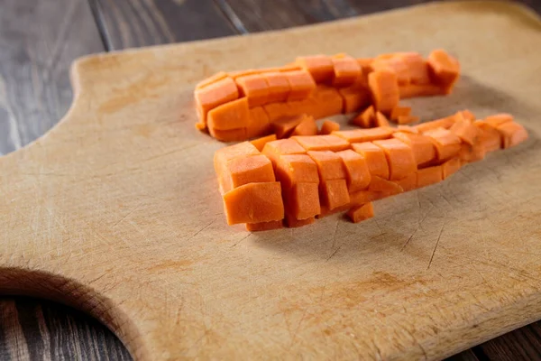 carrot on a cutting board. peeled and diced carrots lie on a cutting board. side view. light wood board.