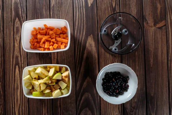 ニンジンのアペソースを作る ミキサーボウル ブラックカラントボウル テーブルの上に野菜と果物のみじん切りの2つの白いボウル ボールの中でダイス リンゴの皮をむいて白いボウルに入れ — ストック写真