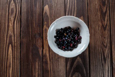 Ahşap bir masada, beyaz bir kasede siyah frenk üzümü. Masada böğürtlen. Sağlıklı kahvaltı. tarım ürünleri.