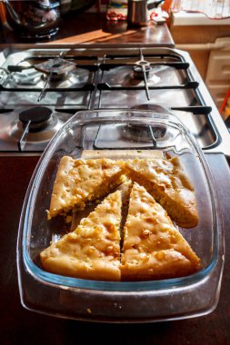 Masanın üzerinde taze yapılmış turta var. Mutfak evin içinde. Ön planda ev yapımı kek, arka planda fırın ve tabaklar. Pencereden güzel bir ışık.