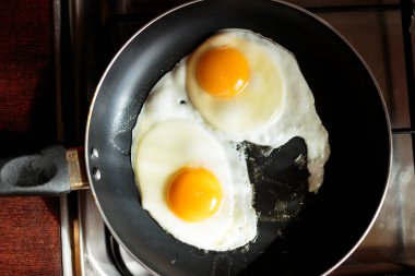 İngiliz kahvaltısı hazırlıyorum. Çırpılmış yumurta pişirmek. Fırındaki tavada iki kırık yumurta var. İki yumurta bir tavada kızarır. Yukarıdan bak. Soba, masa ve kızartma tavası. Mutfak aletleri.