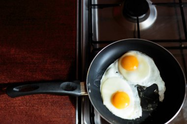 İngiliz kahvaltısı hazırlıyorum. Çırpılmış yumurta pişirmek. Fırındaki tavada iki kırık yumurta var. İki yumurta bir tavada kızarır. Yukarıdan bak. Soba, masa ve kızartma tavası. Mutfak aletleri.