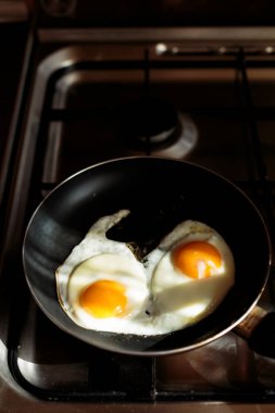 İngiliz kahvaltısı hazırlıyorum. Çırpılmış yumurta pişirmek. Fırındaki tavada iki kırık yumurta var. İki yumurta bir tavada kızarır. Yukarıdan bak. Soba, masa ve kızartma tavası. Mutfak aletleri.