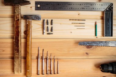 Marangozluk işi. Hafif ahşap arka plan. Ahşap doku. İki çekiç, bir matkap seti, bir kalem, bir demir köşe, bir demir testeresi, bir tornavida. Reklam afişi. Blog için fotoğraf. metin için yer.