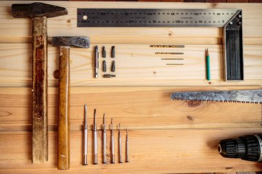 Marangozluk işi. Mobilya üretimi. El işi. Hafif ahşap arka plan. Ahşap doku. İki çekiç, bir matkap seti, bir kalem, bir demir köşe, bir demir testeresi, bir tornavida. Reklam afişi. Blog için fotoğraf. metin için yer.