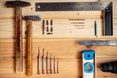 Marangozluk işi. Mobilya üretimi. El işi. Hafif ahşap arka plan. Ahşap doku. İki çekiç, bir matkap seti, bir kalem, bir demir köşe, bir demir testeresi, bir tornavida.