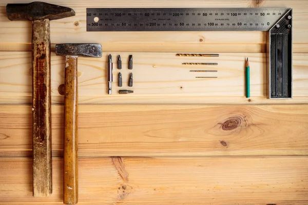 Marangozluk işi. Hafif ahşap arka plan. Ahşap doku. İki çekiç, bir matkap seti, bir kalem ve bir demir köşe tahta arka planda yatıyor. Reklam afişi. Blog için fotoğraf. metin için yer.