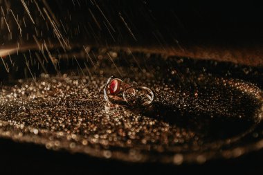 İki halka metal bir tepside küçük su damlaları ile yatar, ayrıca su damlaları yukarıdan gelir; yan görünüm