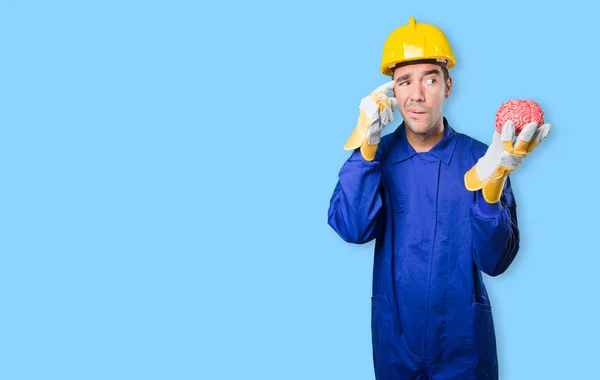 Puzzled workman holding a brain on white background