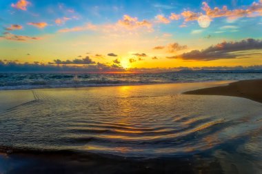 Gün batımında renkli canlı bir deniz manzarası Ön planda su ve Gökyüzünde renkli bulutlar