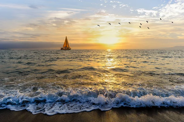 A Sailboat is Sailing Along the Ocean as a Vivid Colorful Sunset is in the Background and Birds Flying