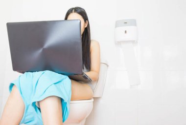 Asyalı kadın mavi şort giyiyordu tuvalette oturmuş evdeki tuvalette dizüstü bilgisayarla çalışıyordu.