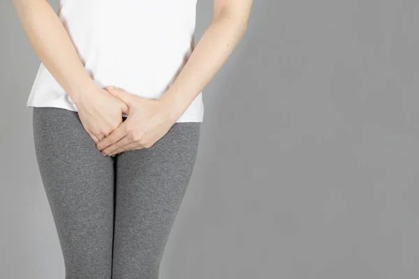 Cropped of woman in gray shorts put her hand on the genitalia area, Penis pain or Itching urinary Health-care concept on gray background