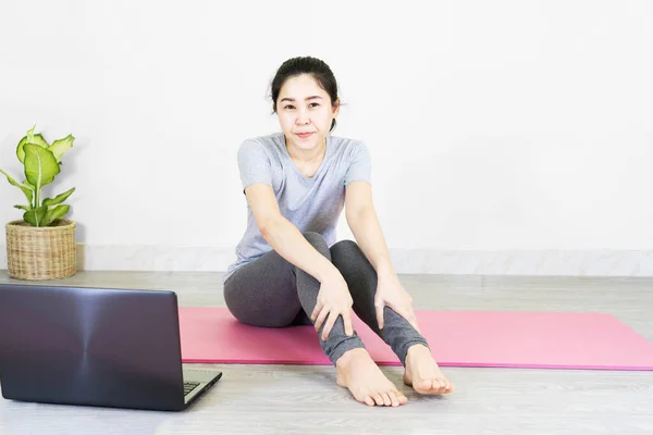 Unhappy young woman sitting on the mat, grabbing an ankle, unable to start yoga work out because of sport injury, feeling pain. Beginner doing wrong exercise without coacher