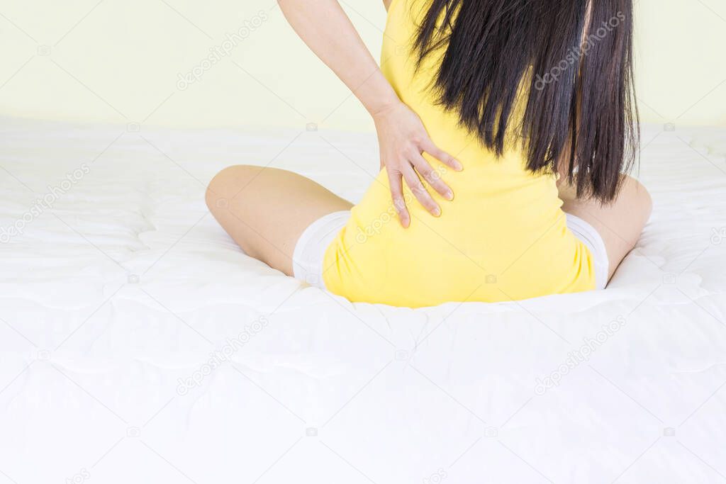 Waist pain, close up of young woman hand holding Back during sitting in the bed room, pain occur before or after sleep
