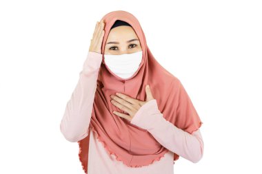 Virüs salgını sırasında tıbbi maske takan geleneksel giysili Asyalı genç bir kadının beyaz arka planda izole edilmiş baş ağrısı var.