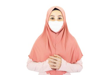 Beyaz arka planda izole edilmiş, geleneksel giysili, tıbbi maske takan genç, güzel, Müslüman bir kadın.