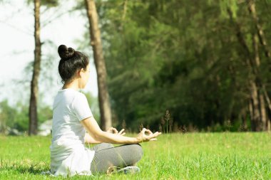Genç ve güzel Asyalı kadın yoga yapıyor ve dışarıda nilüfer çiçeği pozunda meditasyon yapıyor ve kulaklıkla müzik dinliyor. Dışarıda sağlıklı bir yaşam tarzı. Yoga ve rahatlama konsepti.