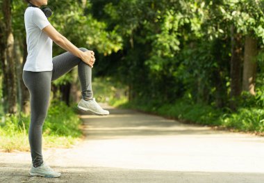 Kadın bacak egzersizi yapıyor, sağlıklı genç kadın koşmadan önce ısınıyor ya da güzel bir yaz gününde parkta koşuyor. Spor fitness antrenmanı konsepti..