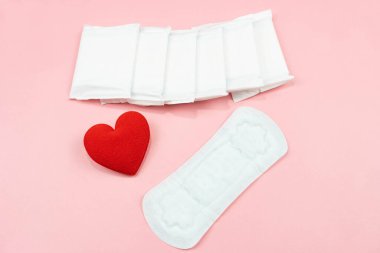 Üst görüş beyaz hijyenik peçete ya da ped ve pembe arka planda kırmızı kalp. Kadın hijyeni, kritik günler kavramı, adet görme, sağlık hizmetleri.