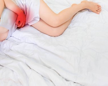 Beyaz uyku giysisi giymiş bir kadın karın ağrısı üzerine yatıyor. Karın ağrıları için el ele tutuşan bir kadın bağırsağında akut iltihap. Acının yerini gösteren okuma noktalı konsept fotoğraf