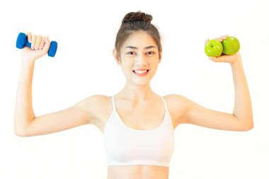 Genç ve güzel Asyalı bir kadın pembe yoga topu, portakal suyu ve mavi dambıl ve yeşil elma ağırlığını kontrol eden ince vücut bakımı ile beyaz atlet egzersizi yapıyor.