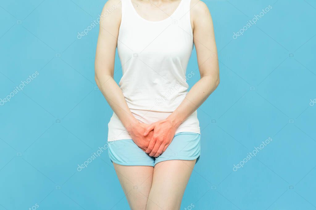 low body of woman feels Penis pain wearing white undershirt standing over isolated blue background with hand holding the crotch because Itching or urinary, painful illness feeling unwell.Ache concept