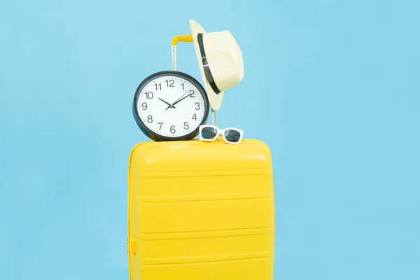 Check in in time before travel, season travel, Summer holidays,vacation duration concept.Yellow Suitcase or luggage bag,clock,sun hat and sunglasses isolated on blue background