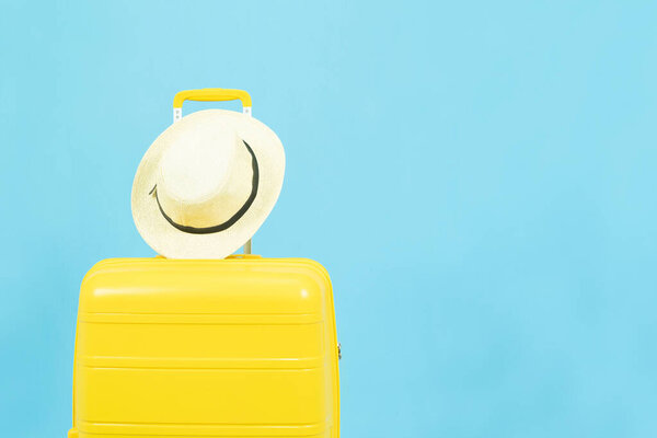 Summer holidays, vacation and travel concept.Yellow Suitcase or luggage bag and sun hat isolated on blue background with copy space