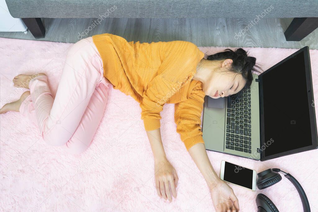 people and leisure concept.Asian young woman working from home under quarantine using a laptop, tired, fatigued,sleepy and falls asleep on pink carpet