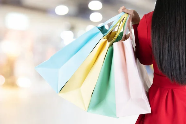 Back of the women long black hair in red dress carrying a lot of colorful shopping bags in blurred shopping mall