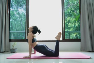 Evde egzersiz yapan kadın, insanlar ve sağlıklı yaşam tarzı konsepti. Spor kıyafetleri giyen kadın yoga yapıyor. Paspasın üzerinde gerinerek kaslarını iyi sağlık ve kilo kaybı için ısıtıyor.