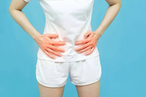 The body of a woman in white clothes put her hands on the Stomach area at spot of ache and mark red, abdominal pain, Health-care concept on blue background with copy space
