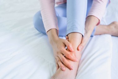 Yatağa yakın oturan kadın ayak bileği incinmiş, acı çekiyor. Sağlık ve tıbbi konsept.