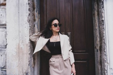 Şehirde beyaz bir binanın yanında kahverengi uzun pantolonlu, modaya uygun güneş gözlüklü Asyalı genç hippi bir kadın duruyor. Yürüyüş için güzel bir kız. Şık kadın kıyafetleri..