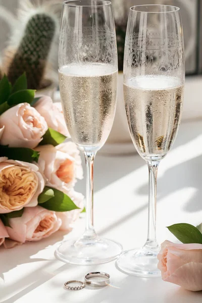 Wedding Rings Lie Next Two Glasses Champagne Bouquet Roses Sun — Stock Photo, Image