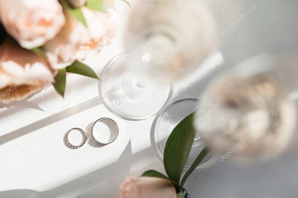 Wedding rings lie next to two glasses of champagne and a bouquet of roses in the sun
