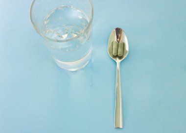 Kaşığın üzerine haplar ve yanına da bir bardak su. Tıbbi ya da sağlık odaklı resim için kullanılır. Kapsüllerdeki klorella süper yiyecekler. Sebze Yemi Klorella.