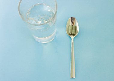 Kaşığın üzerine haplar ve yanına da bir bardak su. Tıbbi ya da sağlık odaklı resim için kullanılır. Kapsüllerdeki klorella süper yiyecekler. Sebze Yemi Klorella.