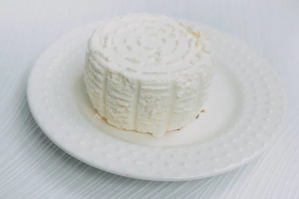 Queso casero en un plato blanco sobre un fondo blanco. queso adighe de la leche. Fabricación casera de queso —  Fotos de Stock